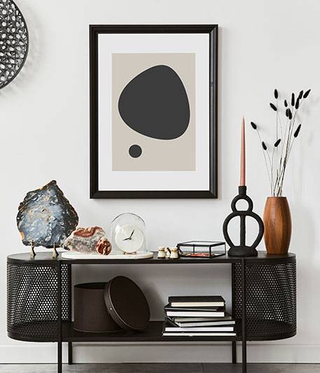 özel ölçü mutfak dolabı Taş levha, saat, kitaplar, mum, vazolar ve masanın üzerindeki beyaz duvara asılı siyah çerçeveli soyut sanat eserleri gibi dekoratif öğeler içeren modern bir mobilya konsol masası. dolap